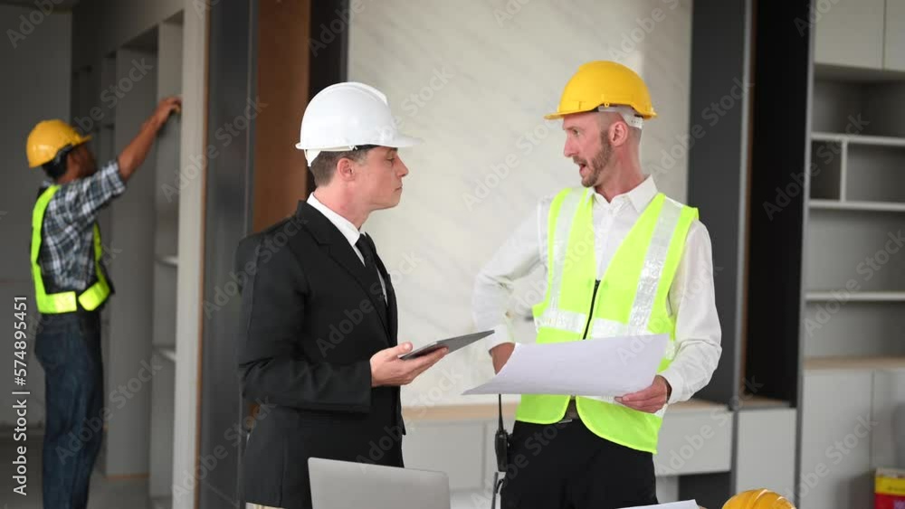 Contractor and architect looking at plan, tablet, laptop and talking about working on big project. Building in construction interior.. Contractor and architect looking at plan, tablet, laptop and talking about working on big project. Building in construction interior..
