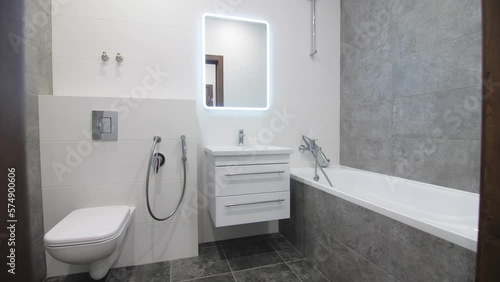 Stylish renovated bathroom with bathtub and toilet bowl in apartment. Elegant minimal interior of rest room with grey tiles
