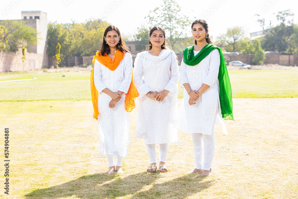 Indian Independence day or Republic day concept. Three young beautiful woman wearing traditional white dress standing at park looking at camera. Full length shot. Indian Independence day or Republic day concept. Three young beautiful woman wearing traditional white dress standing at park looking at camera. Full length shot.