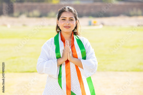 Portrait of young indian woman wearing traditional white kurta and tricolor duppata do namaste while standing at park. Election and politics, celebrating Independence day or Republic day.