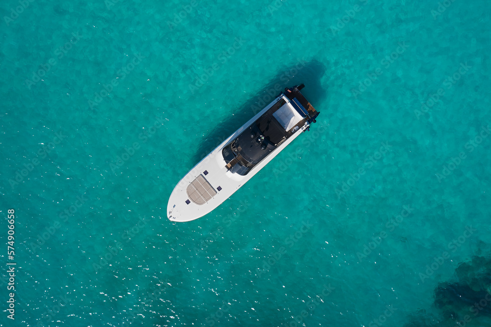 Fototapeta premium Big white motor boat anchored in the blue sea top view. White modern boat with motor on blue transparent water aerial view.