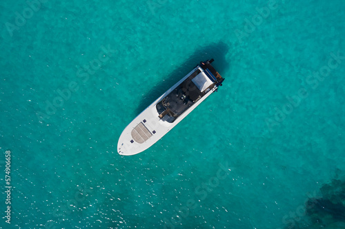 Big white motor boat anchored in the blue sea top view. White modern boat with motor on blue transparent water aerial view.