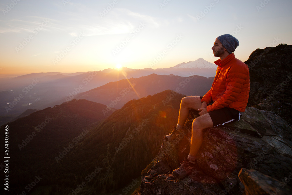 A hiker watches the sunset from a rocky cliff bluff on the summit of Sauk Mountain. A hiker watches the sunset from a rocky cliff bluff on the summit of Sauk Mountain.