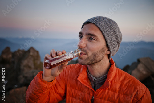 A man enjoys a swig of whiskey after hiking to the summit of a mountain.