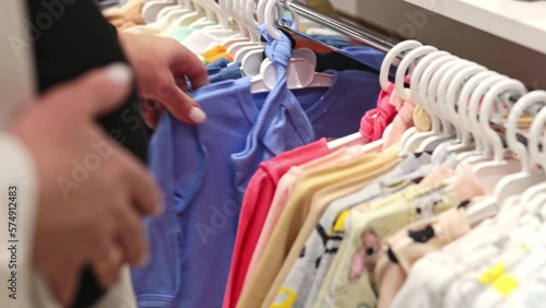 A woman chooses children's clothes in a children's clothing store. Pregnancy and shopping