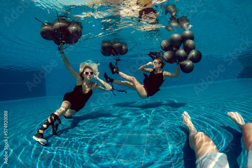 Underwater shoot of flying two women with black balloons