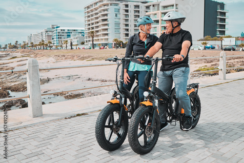 Senior couple, electric bike and ride by the beach for fun bonding activity or travel together in the city. Happy elderly man and woman enjoying cruise on electrical bicycle for trip in Cape Town