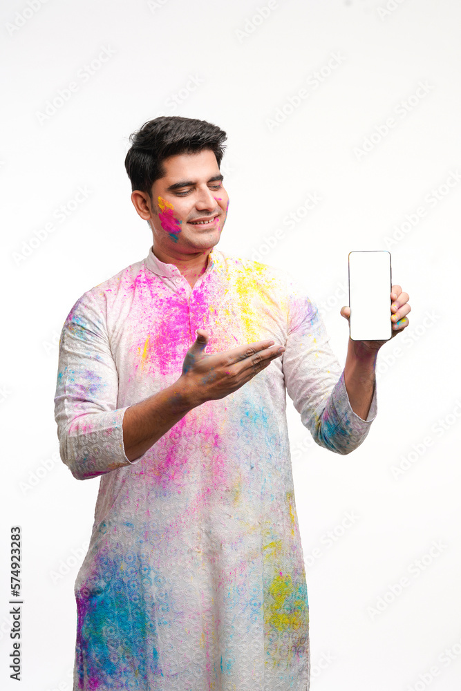 Indian man showing mobile screen on holi festival with face painted and in traditional wear. Indian man showing mobile screen on holi festival with face painted and in traditional wear.