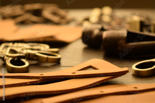 Leather workshop, handbag or shoe manufacturing industry, hand craft. Numerous metal elements bag hardware indoors. Leather pieces on wooden table. Work tools for leather handicraft. Closeup view.