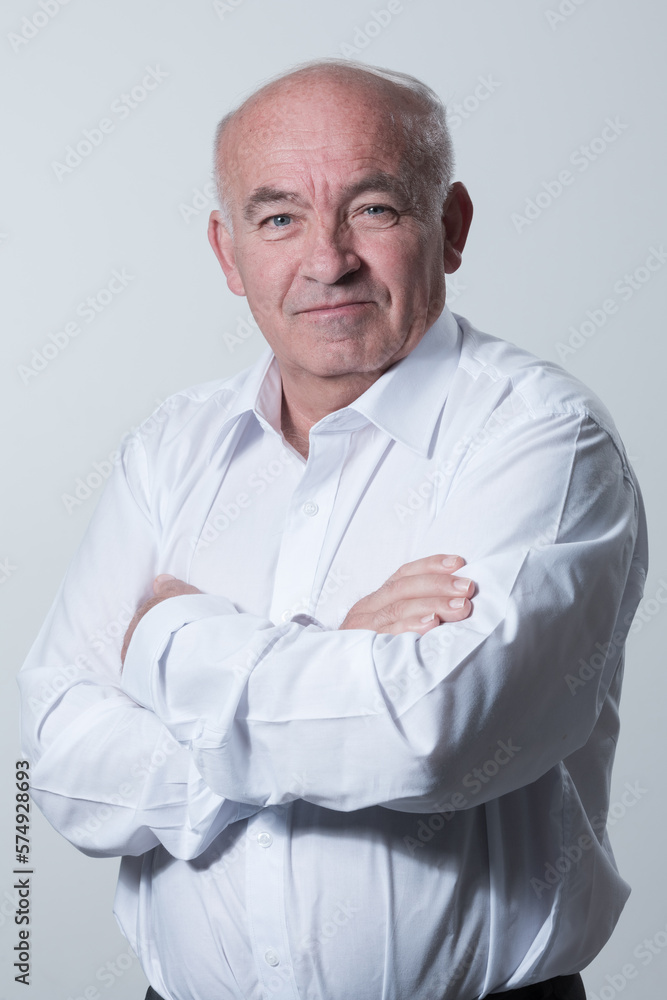 Confident senior man in white shirt crossing hands on chest and looking at camera while standing against gray background. Self confident senior isolated white studio shoot. Confident senior man in white shirt crossing hands on chest and looking at camera while standing against gray background. Self confident senior isolated white studio shoot.