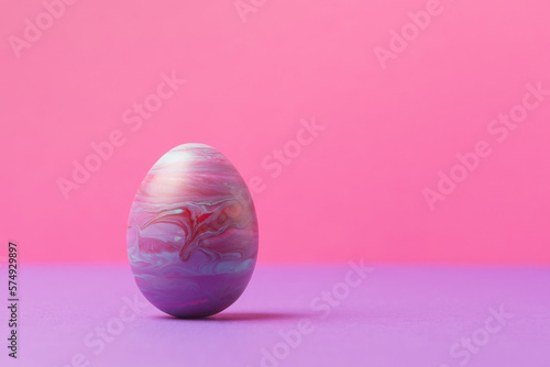 Decorative Easter egg painted in fluid art technique against pink background with copy space. Easter holiday greeting concept