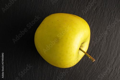 One yellow organic apple on slate stone, macro, top view. photo