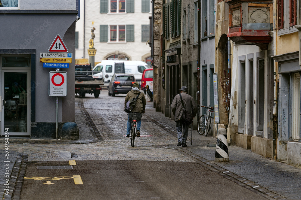 Senior man with hat and walking stick at alley and male cyclist at the old town of Swiss City of Schaffhausen on a foggy winter day. Photo taken February 16th, 2023, Schaffhausen, Switzerland.
