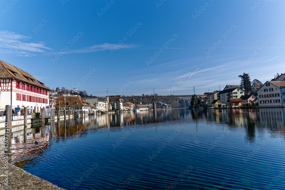 Scenic view of Rhine River at City of Schaffhausen with railway bridge and village of Feuerthalen in the background on a sunny winter day. Photo taken February 16th, 2023, Schaffhausen, Switzerland.