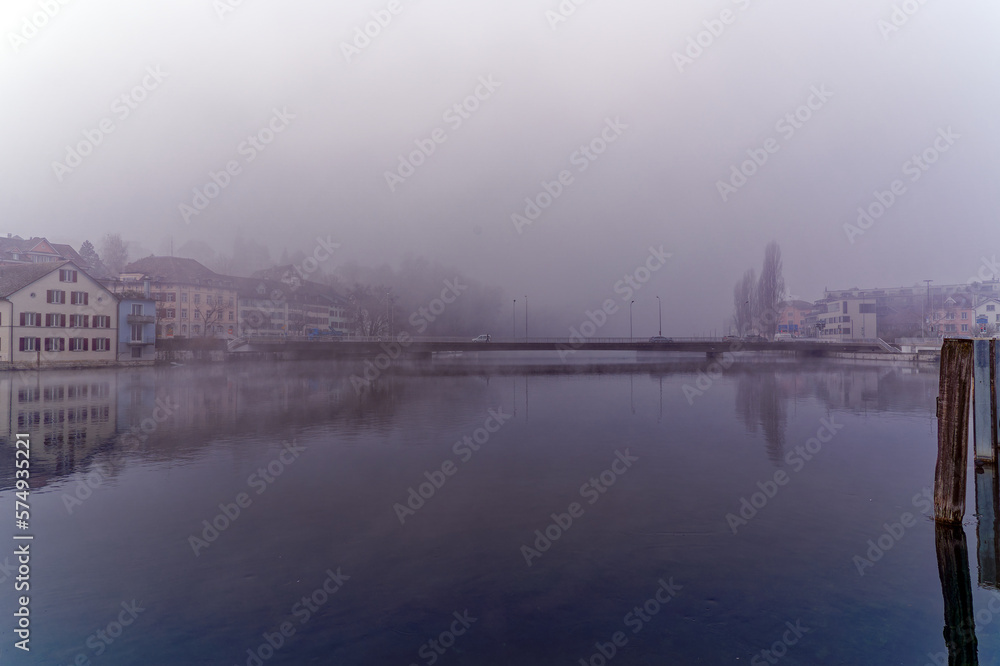 Naklejka premium Scenic view of Rhine River with car bridge an village Feuerthalen in the background on a foggy winter day. Photo take February 16th, 2023, Schaffhausen, Switzerland.