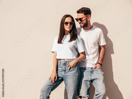 Smiling beautiful woman and her handsome boyfriend. Woman in casual summer jeans clothes. Happy cheerful family. Female having fun. Sexy couple posing in the street near wall. In sunglasses