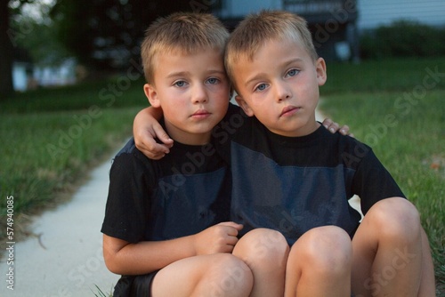 Portrait of twin brothers sitting on a street curb with their arms around each other, Lena, Illinois, USA photo