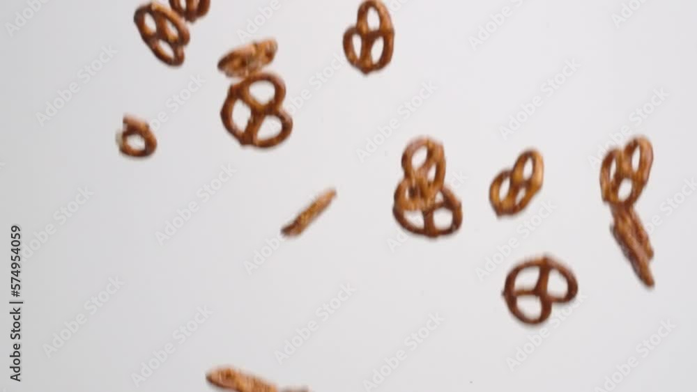 Salty twisted pretzel snack crackers raining down and bouncing on white backdrop in slow motion Salty twisted pretzel snack crackers raining down and bouncing on white backdrop in slow motion