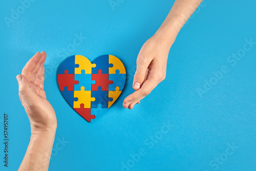 Father and autistic son hands holding jigsaw puzzle heart shape. World Autism Awareness Day