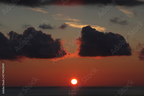 Sunset over the sea with a round sun on the horizon of red sky and black clouds