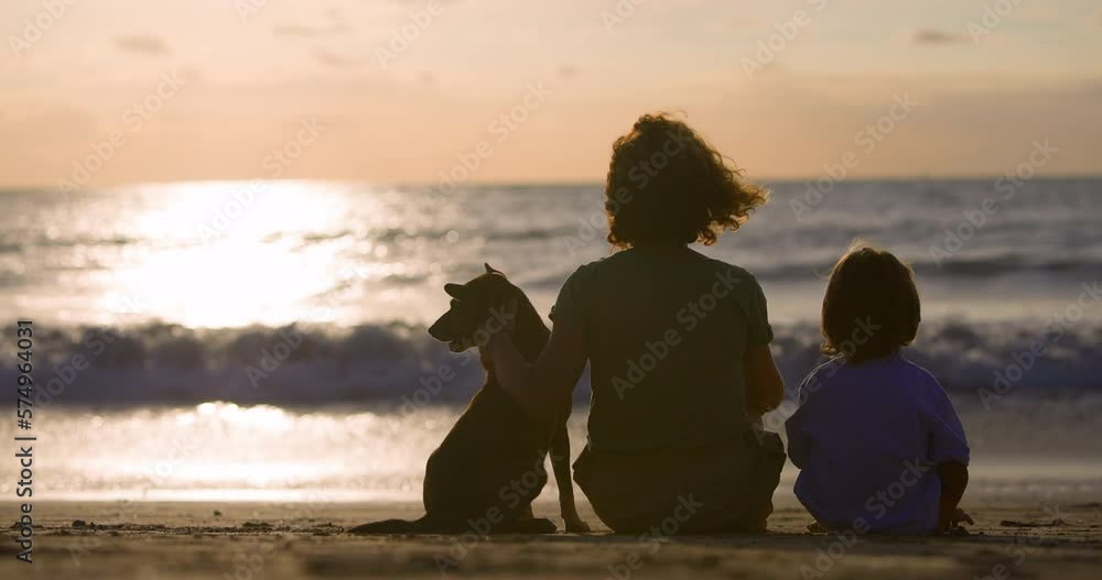 Family of mom, only child and their faithful dog relax on beach after active day filled with fun and games. Sea waves shine beautifully in sun, attracting eye. Family contemplative rest on coastline Family of mom, only child and their faithful dog relax on beach after active day filled with fun and games. Sea waves shine beautifully in sun, attracting eye. Family contemplative rest on coastline