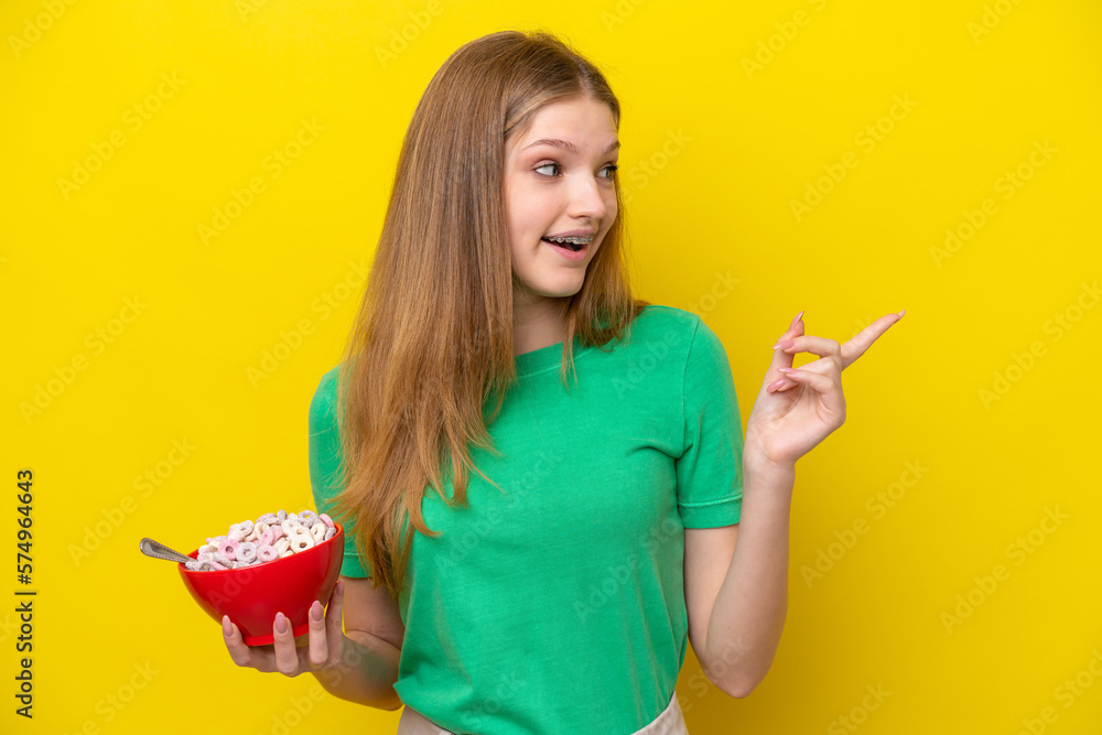 Teenager Russian girl holding bowl of cereals isolated on yellow background intending to realizes the solution while lifting a finger up Teenager Russian girl holding bowl of cereals isolated on yellow background intending to realizes the solution while lifting a finger up