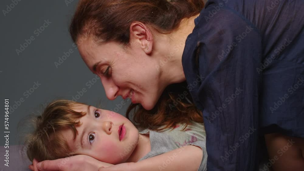 Close up shot of young mother is playing and kiss with her little girl in in a morning on gray background. Concept of children, baby, parenthood, childhood, life, maternity, motherhood Close up shot of young mother is playing and kiss with her little girl in in a morning on gray background. Concept of children, baby, parenthood, childhood, life, maternity, motherhood