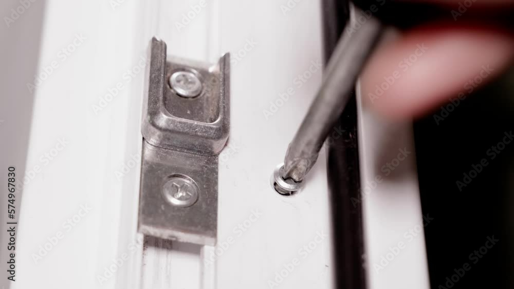 Screwing a self-tapping screw into the body of a plastic door close-up. Final assembly of white plastic doors or windows. Curly Phillips screwdriver screwing the screw Screwing a self-tapping screw into the body of a plastic door close-up. Final assembly of white plastic doors or windows. Curly Phillips screwdriver screwing the screw