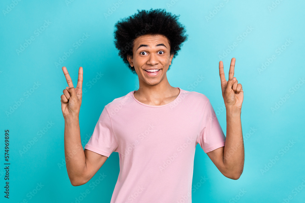 Photo portrait of youngster funky guy big chevelure hair wear stylish pink t-shirt show v-sign friendly vibe isolated on aquamarine color background Photo portrait of youngster funky guy big chevelure hair wear stylish pink t-shirt show v-sign friendly vibe isolated on aquamarine color background