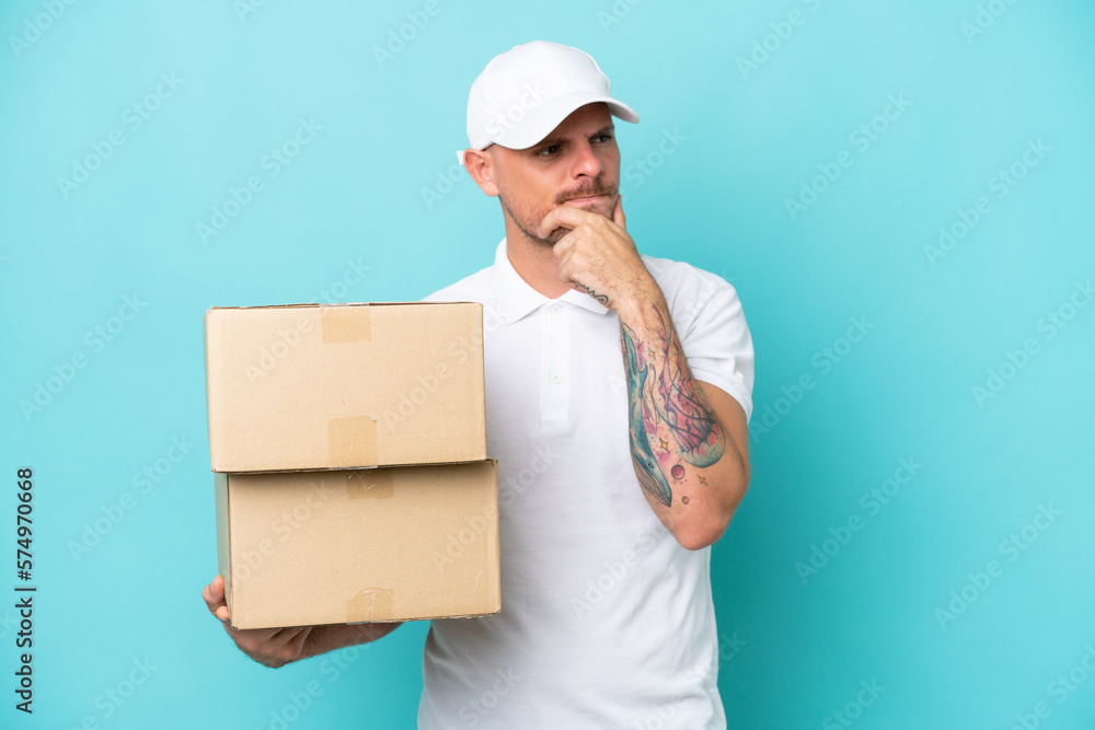 Delivery caucasian man isolated on blue background having doubts and thinking Delivery caucasian man isolated on blue background having doubts and thinking