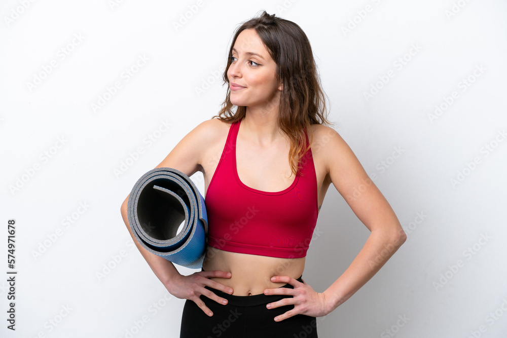 Young sport caucasian woman going to yoga classes while holding a mat isolated on white background posing with arms at hip and smiling Young sport caucasian woman going to yoga classes while holding a mat isolated on white background posing with arms at hip and smiling