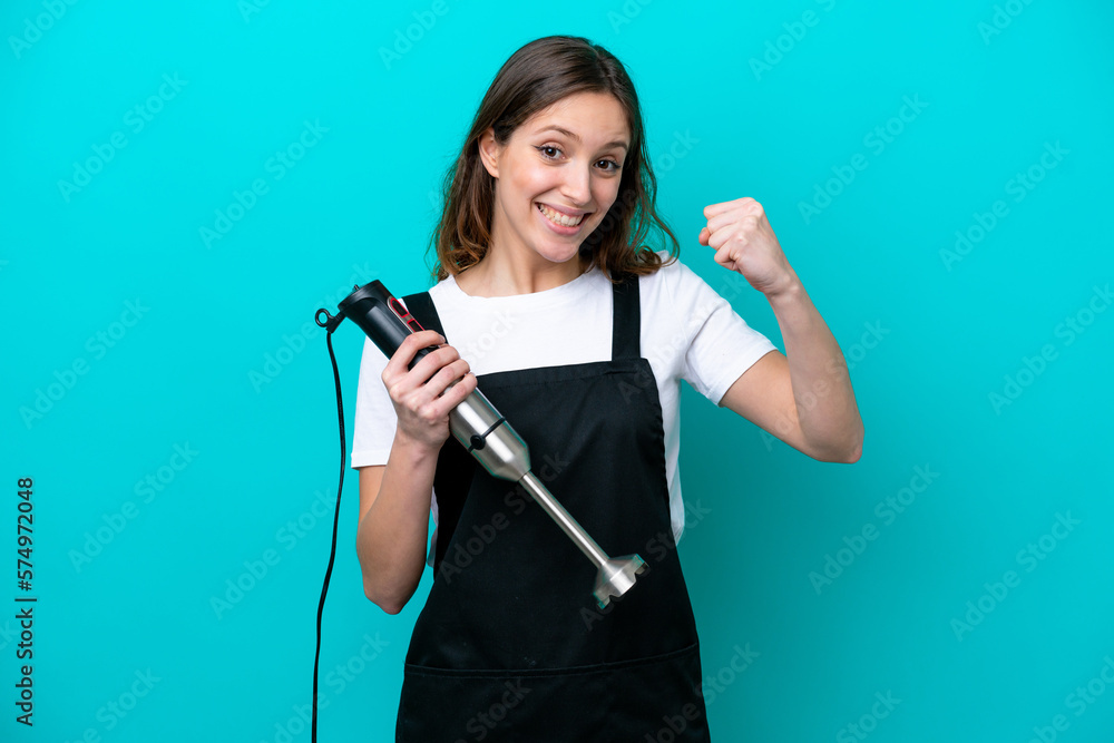 Young caucasian cooker woman using hand blender isolated on blue background celebrating a victory in winner position Young caucasian cooker woman using hand blender isolated on blue background celebrating a victory in winner position