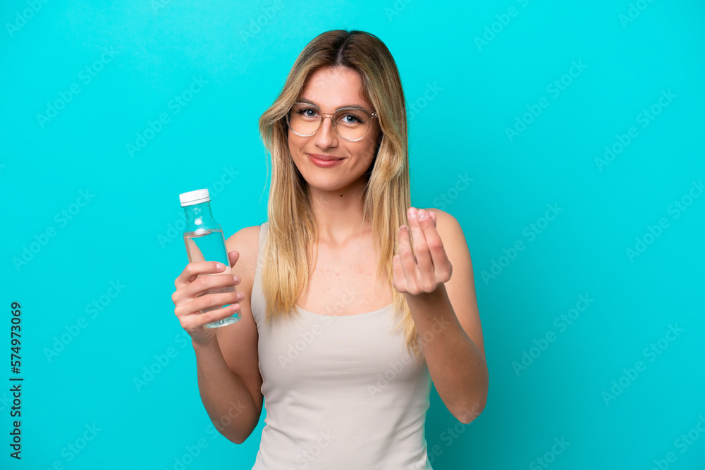 Young Uruguayan woman with a bottle of water isolated on blue background making money gesture Young Uruguayan woman with a bottle of water isolated on blue background making money gesture