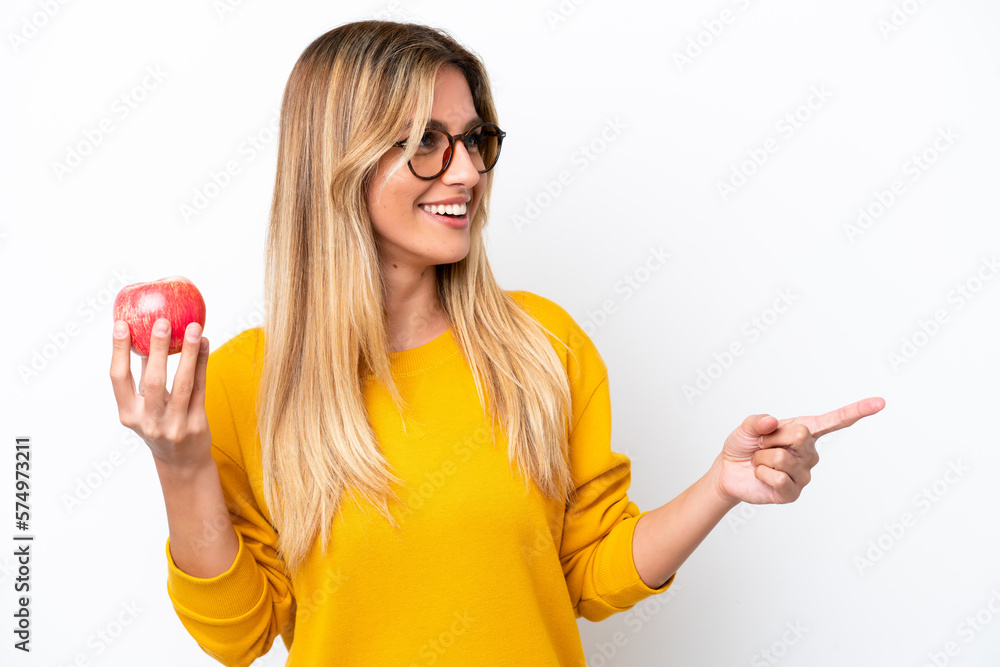 Young Uruguayan woman with an apple isolated on white background pointing to the side to present a product Young Uruguayan woman with an apple isolated on white background pointing to the side to present a product