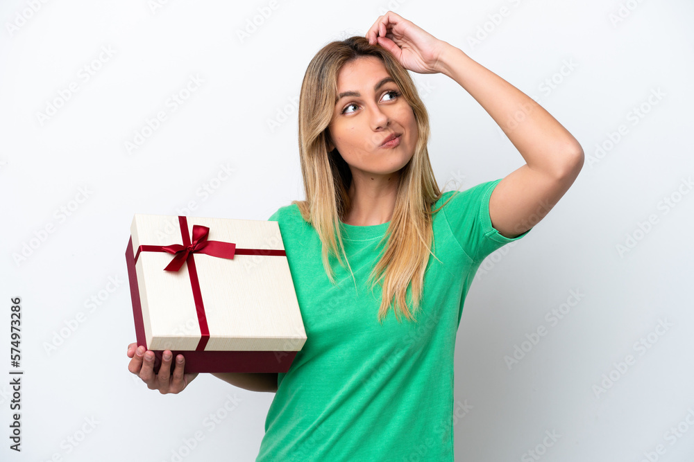 Young Uruguayan woman holding a gift isolated on white background having doubts and with confuse face expression Young Uruguayan woman holding a gift isolated on white background having doubts and with confuse face expression