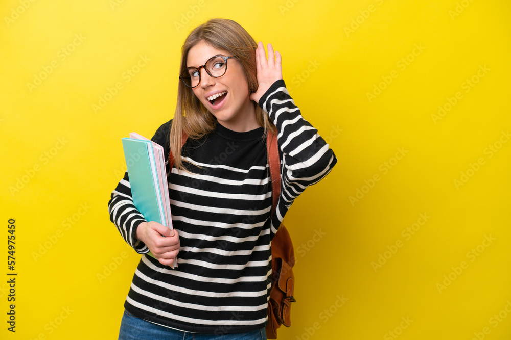 Young student woman isolated on yellow background background listening to something by putting hand on the ear Young student woman isolated on yellow background background listening to something by putting hand on the ear