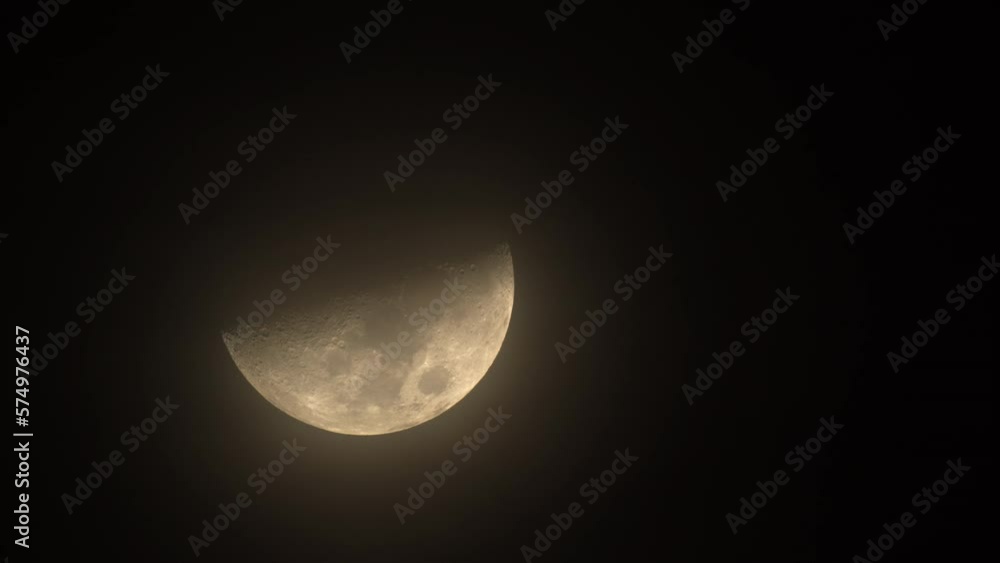 Long telephoto shot capturing half of a moon moving slowly in a dark sky Long telephoto shot capturing half of a moon moving slowly in a dark sky