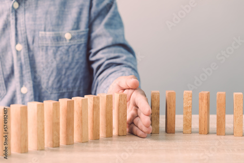 Businessman's hand stopping wooden block as domino on the desk. Ideas of business crisis effect or risk situation protection concect. photo