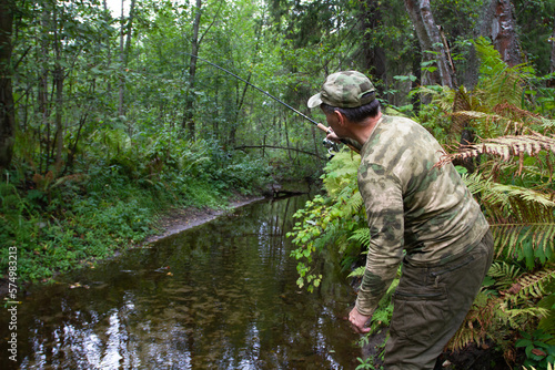 a angler is fishing with a spinning rod on a small forest river