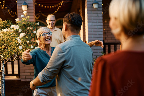 Happy senior woman welcoming her son and his wife in front of her home.