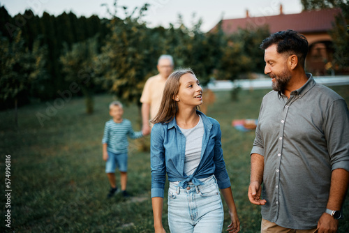 Happy father and daughter talk while walking in backyard.