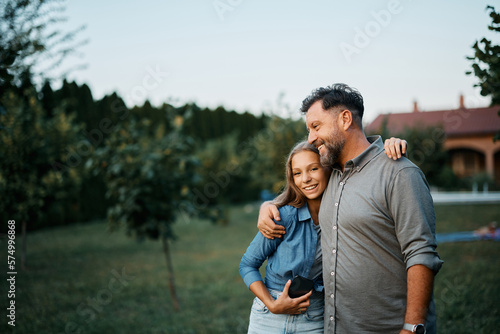 Happy teenage girl hugs her father in backyard and looking at camera.