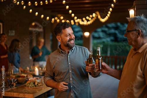 Happy man and his senior father toast with beer during family gathering on patio.