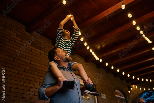 Foto Happy father carrying his son on his shoulders while turning on lightbulb on patio