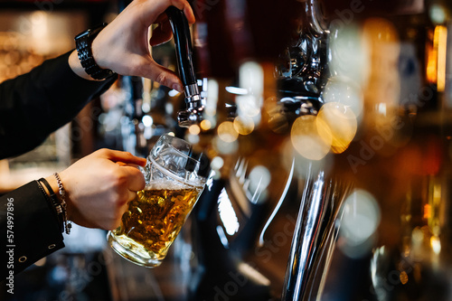 man bartender hand at beer tap pouring a draught beer in glass serving in a restaurant or pub