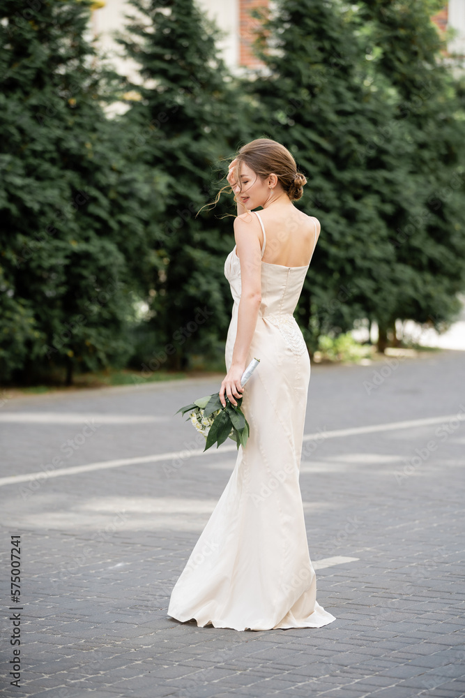 full length of happy bride in white dress holding wedding bouquet and standing on street. full length of happy bride in white dress holding wedding bouquet and standing on street.