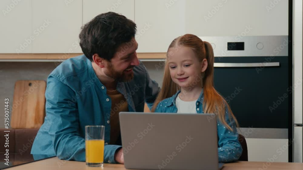 Adult dad explain teaching small kid girl help with using laptop at home kitchen. Daughter learning typing surfing browsing internet with parental control using modern computer together with father Adult dad explain teaching small kid girl help with using laptop at home kitchen. Daughter learning typing surfing browsing internet with parental control using modern computer together with father