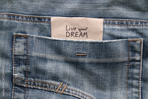 Live your dream. Motivational quotes inscription on a tag in a pocket of blue jeans.