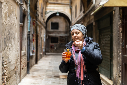 Young woman in winter clothes holding a glass of liquor Aperol Spritz on the streets of Venice, Italy © cabuscaa