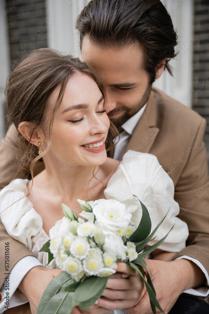 bearded groom hugging happy bride in white dress with wedding bouquet. bearded groom hugging happy bride in white dress with wedding bouquet.